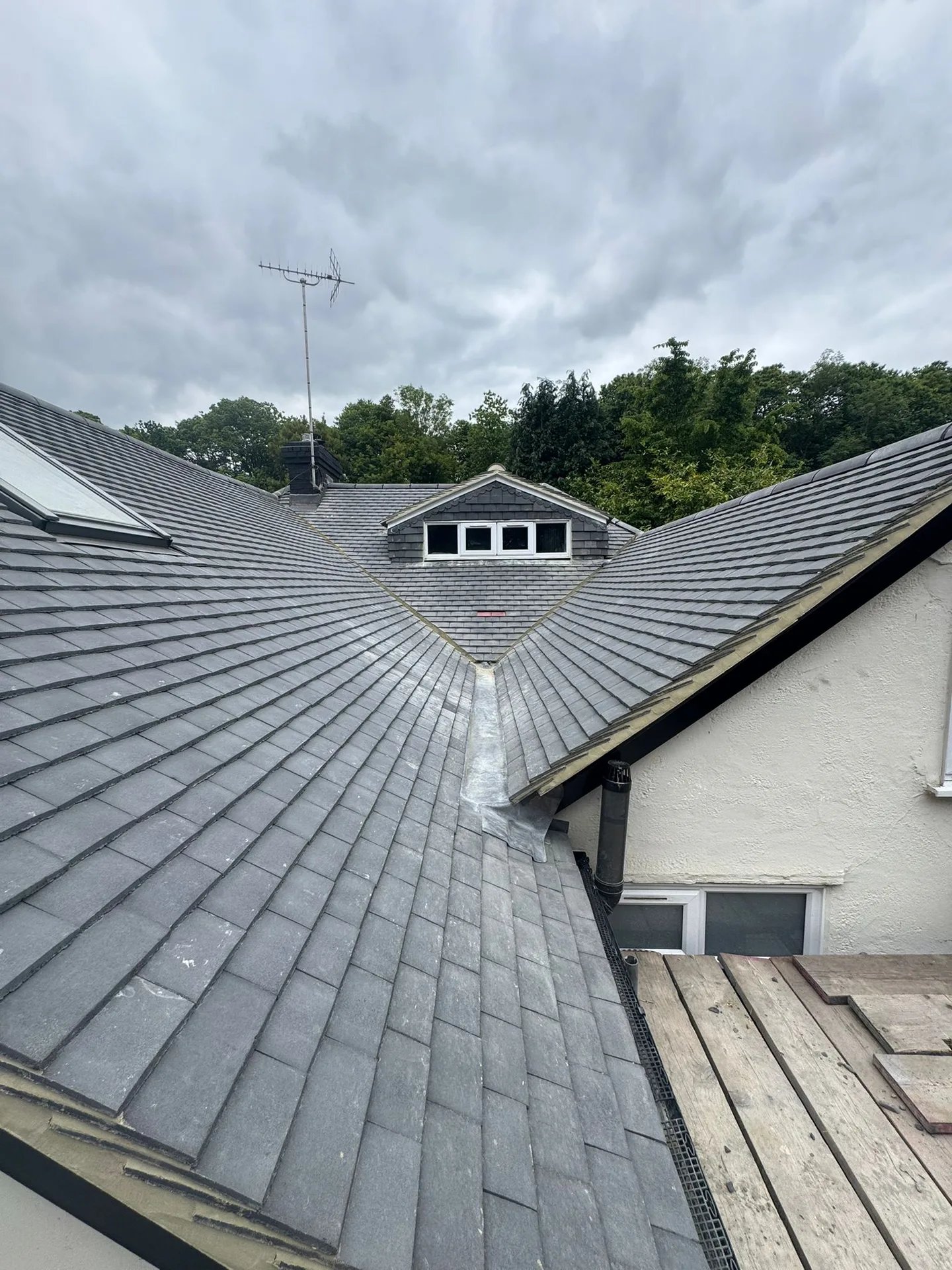 Newly tiled grey roof with a hip and valley, seen from the scaffold