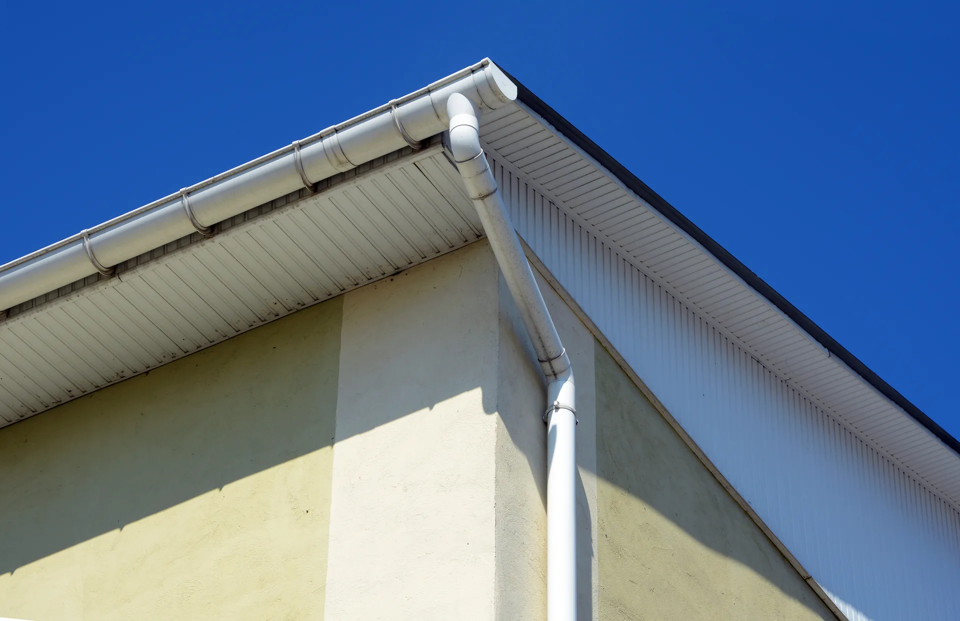 White fascia, soffit and gutter on the corner of a house against a deep blue sky