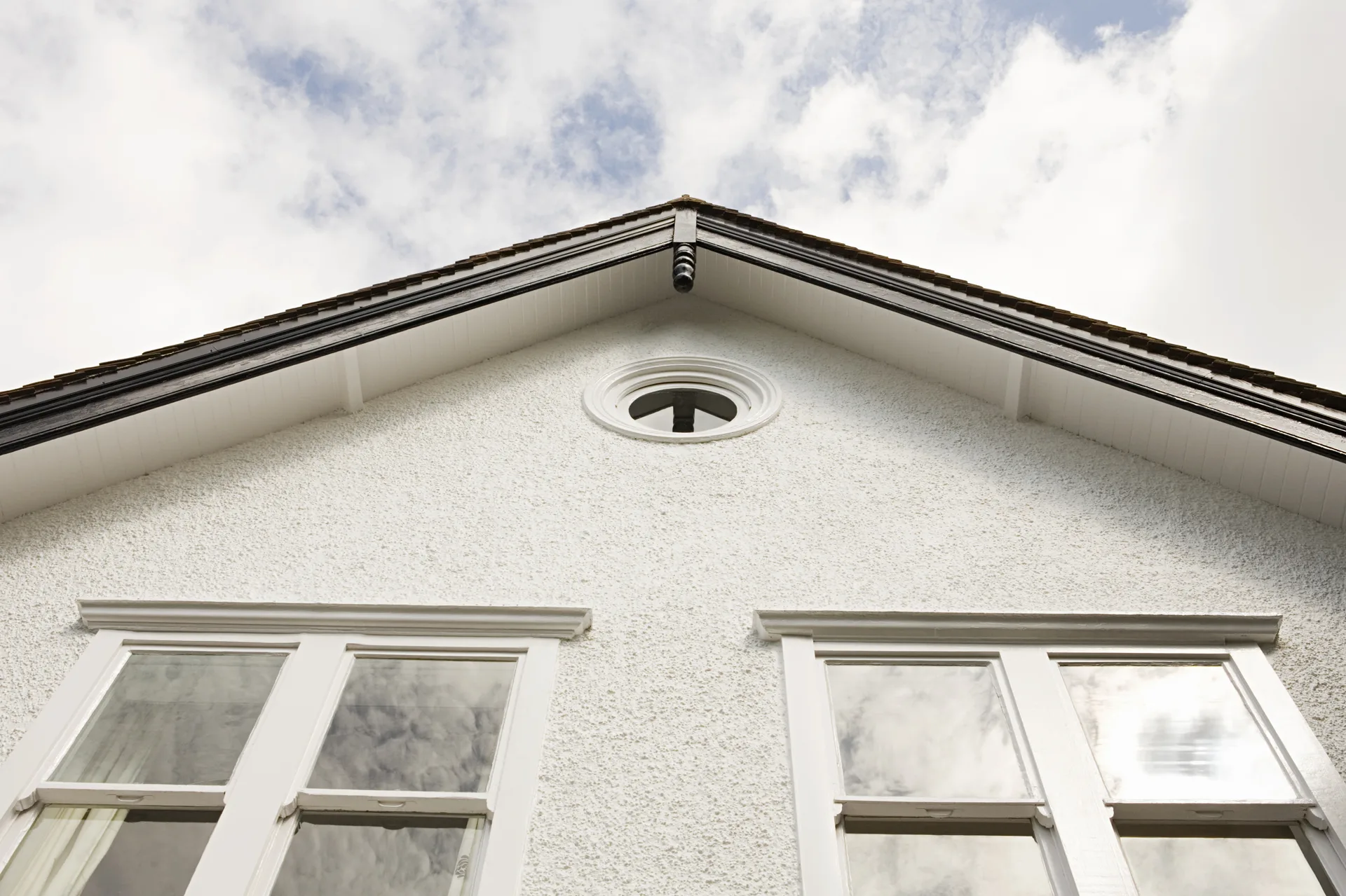 Freshly rendered white gable wall with a round vent and new windows